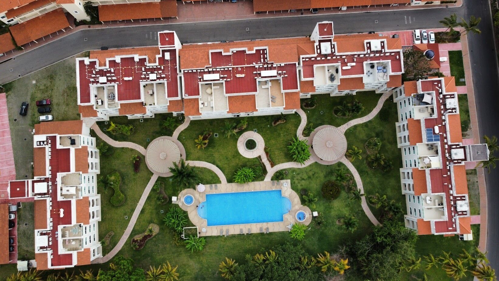 Eine Vogelperspektive eines Hotels mit mehreren Gebäuden, einem zentral gelegenen Schwimmbad und angelegten Gärten.