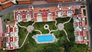 Vista aérea de un hotel con varias edificaciones, una piscina central y jardines ajardinados.
