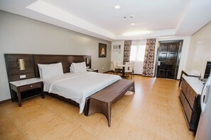 Une chambre d’hôtel moderne dotée d’un grand lit, d’une table de chevet, d’un banc, d’un bureau avec des chaises et d’une armoire.