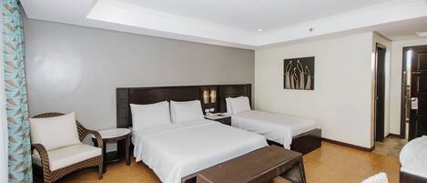 A hotel room with two beds, a sitting area with a chair and table, and a wooden floor.