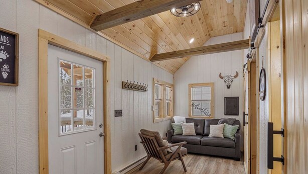 A cozy living room with a wooden ceiling, a sofa, a chair, and a door with a coat rack. - Hill Side Suite (Little Valley)
