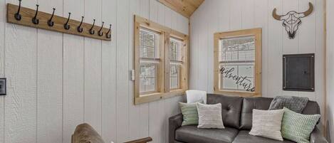 A cozy room with a wooden ceiling, a leather sofa with cushions, a wooden chair, and a wall-mounted coat rack.