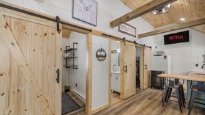 A wooden interior with a sliding door, a welcome sign, a Netflix sign, and a kitchen area with stools. - Hill Side Suite (Little Valley)