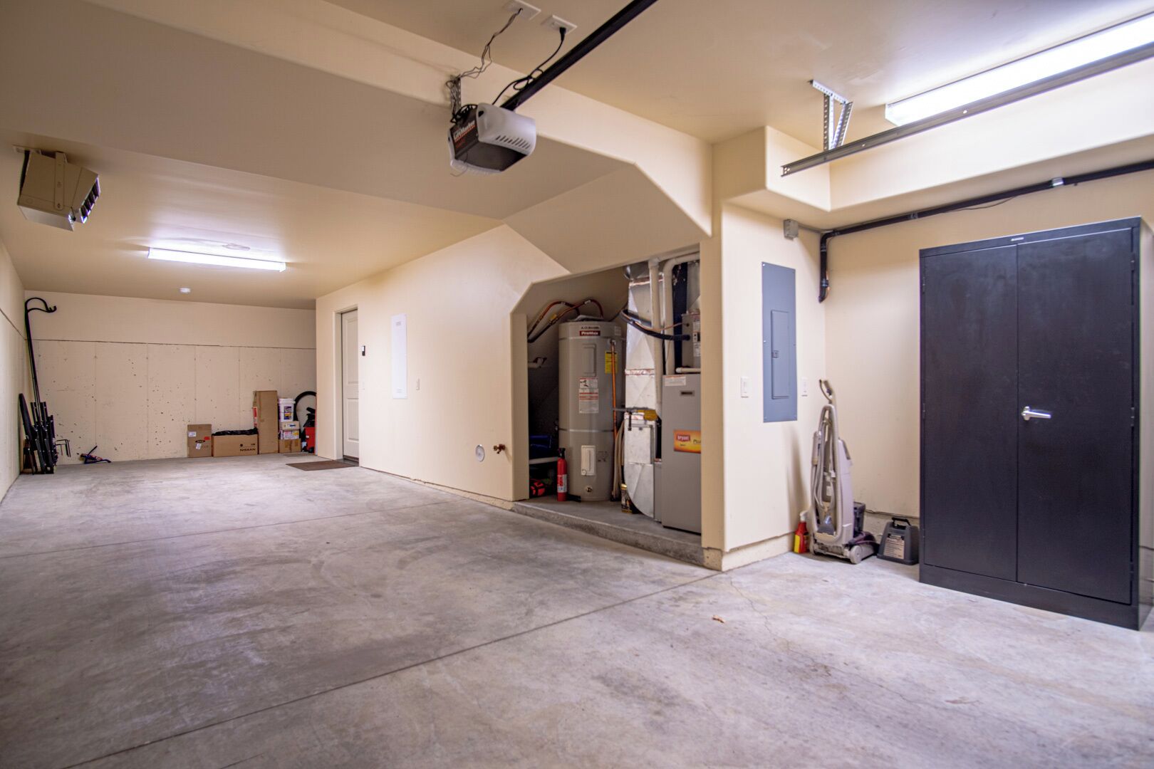 A spacious garage with concrete floors, a large black door, and a ceiling-mounted projector.