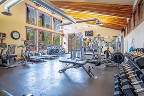 A gym with various exercise equipment, large windows, and a wooden ceiling.
