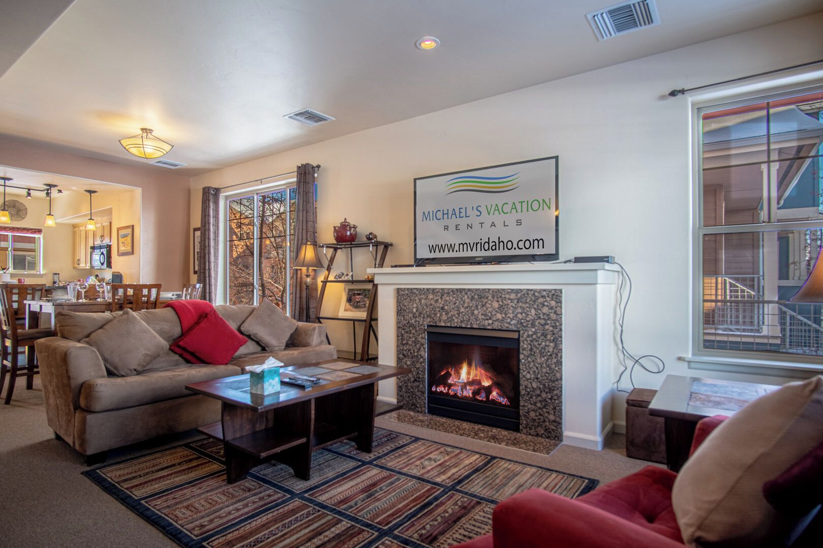 A cozy living room with a fireplace, a dining area, and a kitchen visible through an open door.