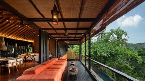 A modern room with a wooden floor, a sofa, a dining table, and a view of lush greenery.