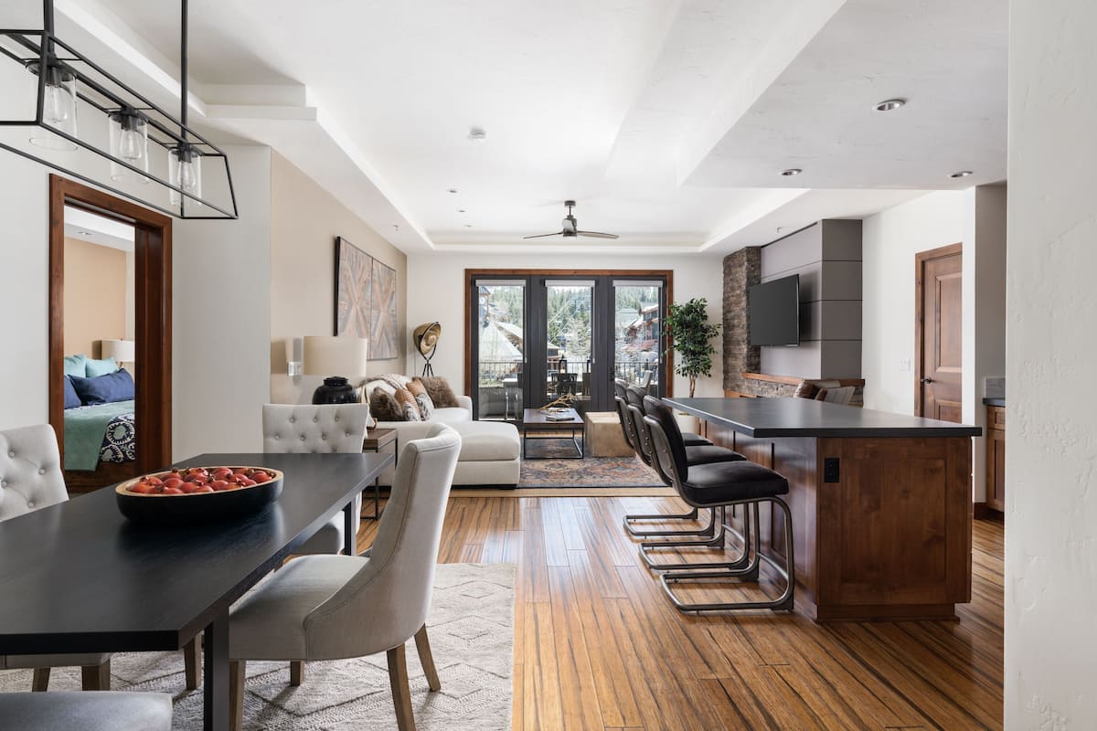 A modern kitchen with a central island, dining area with a dark table, and a living room with a sofa and chairs.