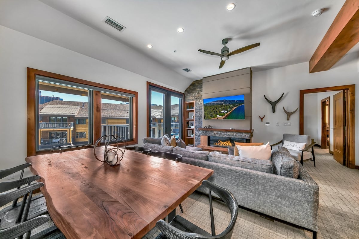 A spacious living area with a wooden dining table, gray sofa, and a mounted TV.