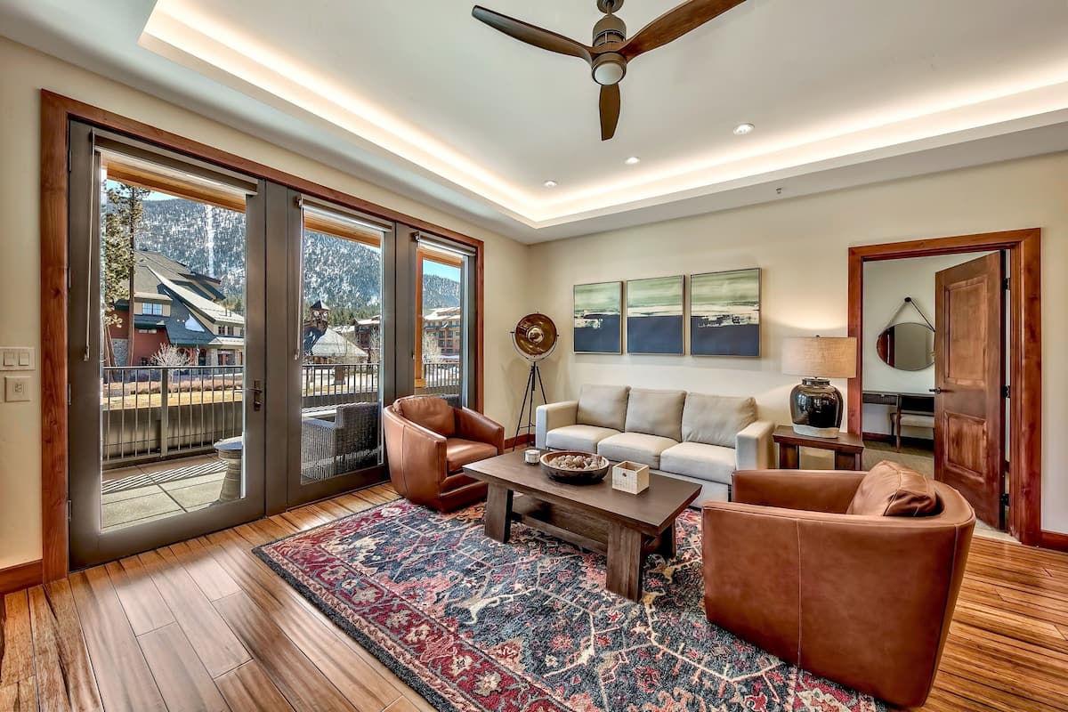 A spacious living room with a large wooden coffee table, leather armchairs, a white sofa, and a patterned rug.