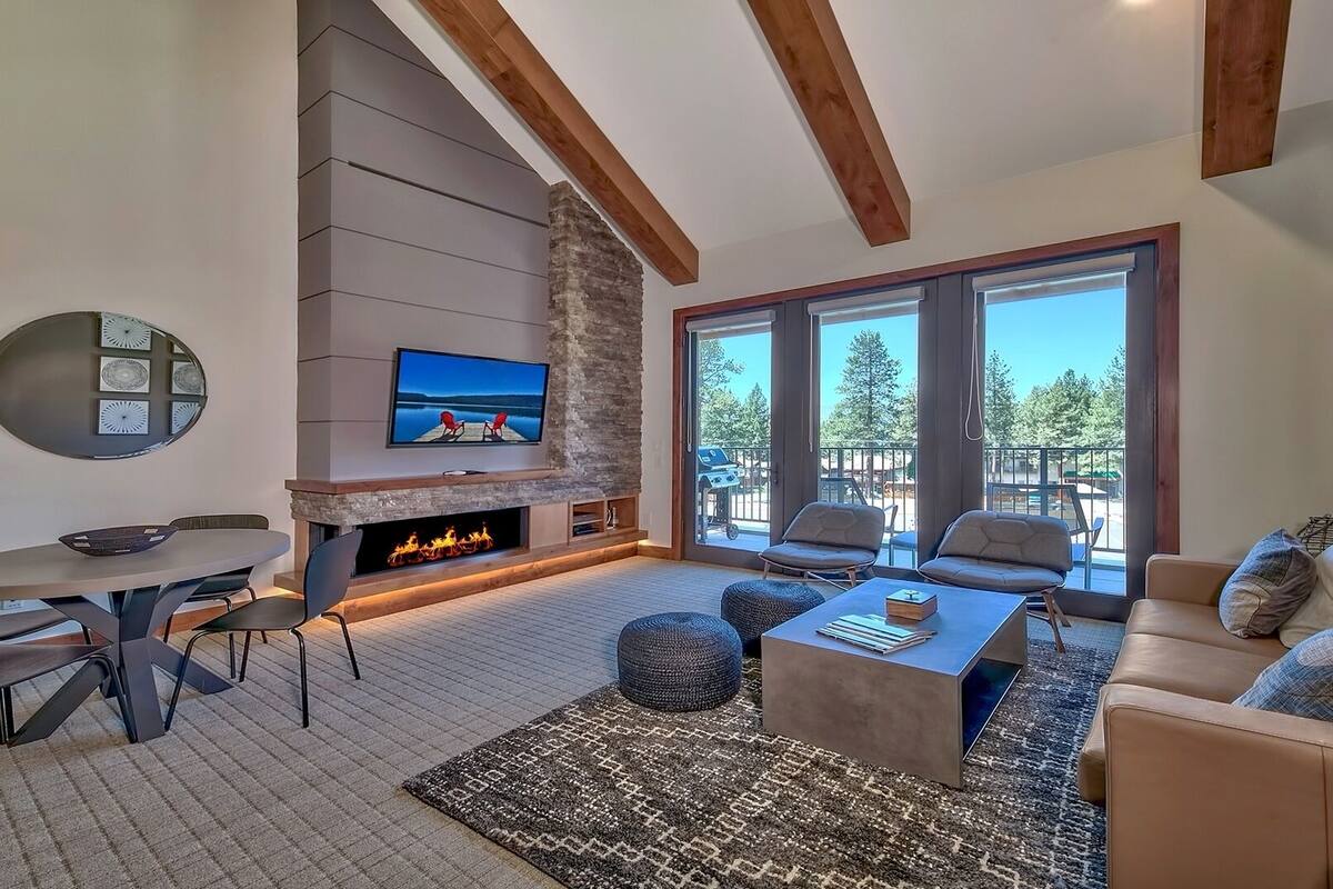 A modern living room with a stone fireplace, a dining area, and a large window offering a view of the outdoors.