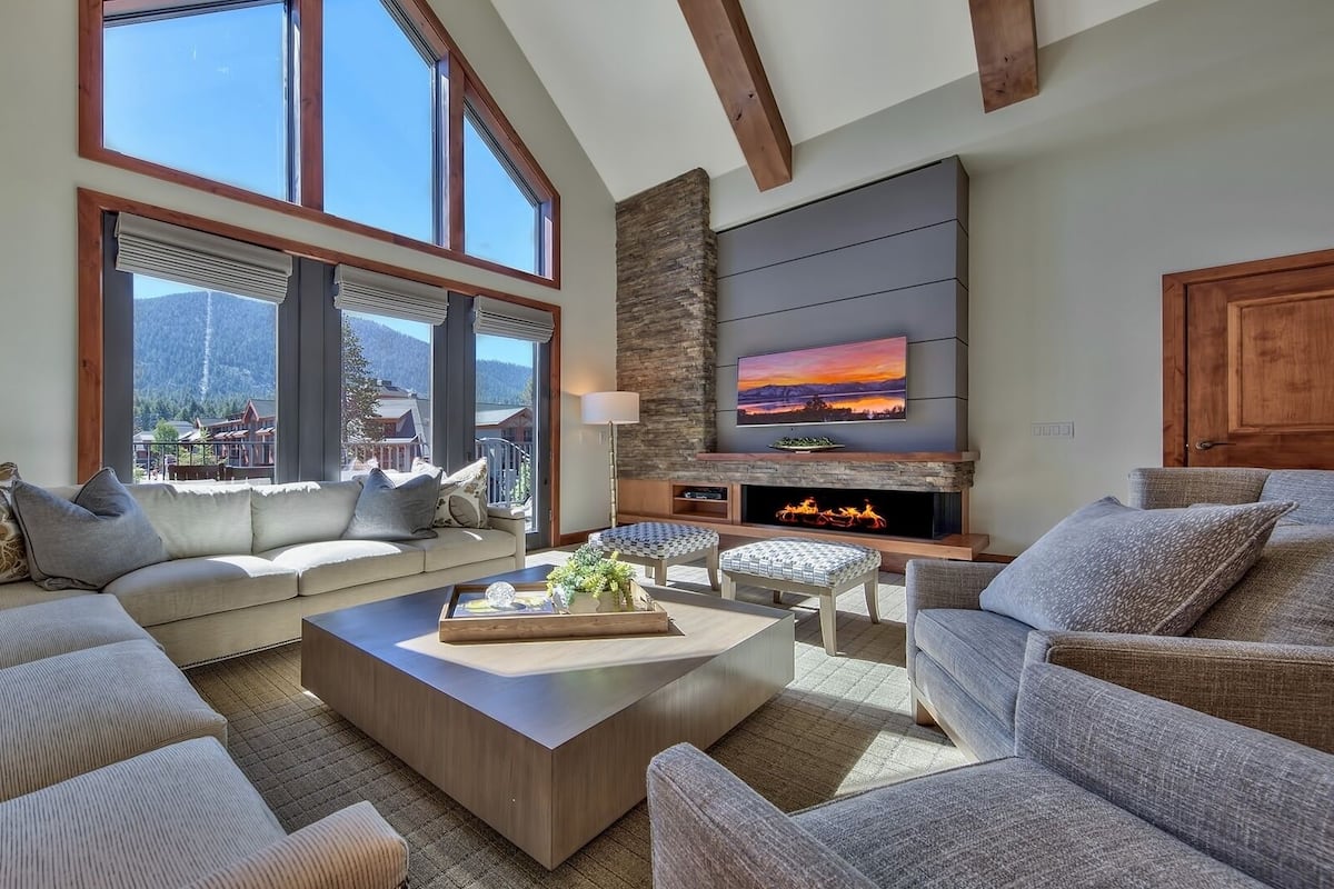 A spacious living room with a large window, a fireplace, and a flat-screen TV mounted on the wall.