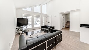 A spacious living room with a large TV, black leather sofas, and a glass coffee table.