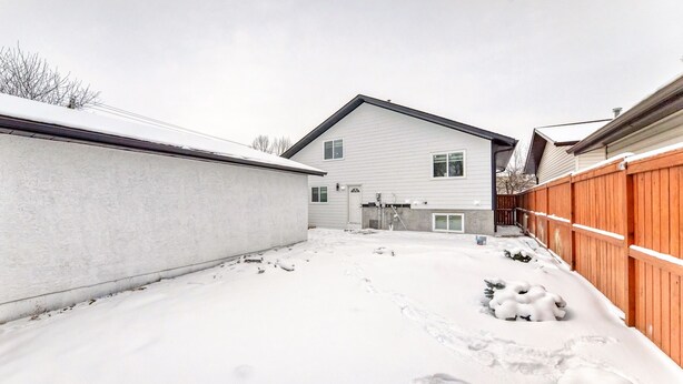 A snow-covered backyard with a house, a wooden fence, and a concrete wall.
