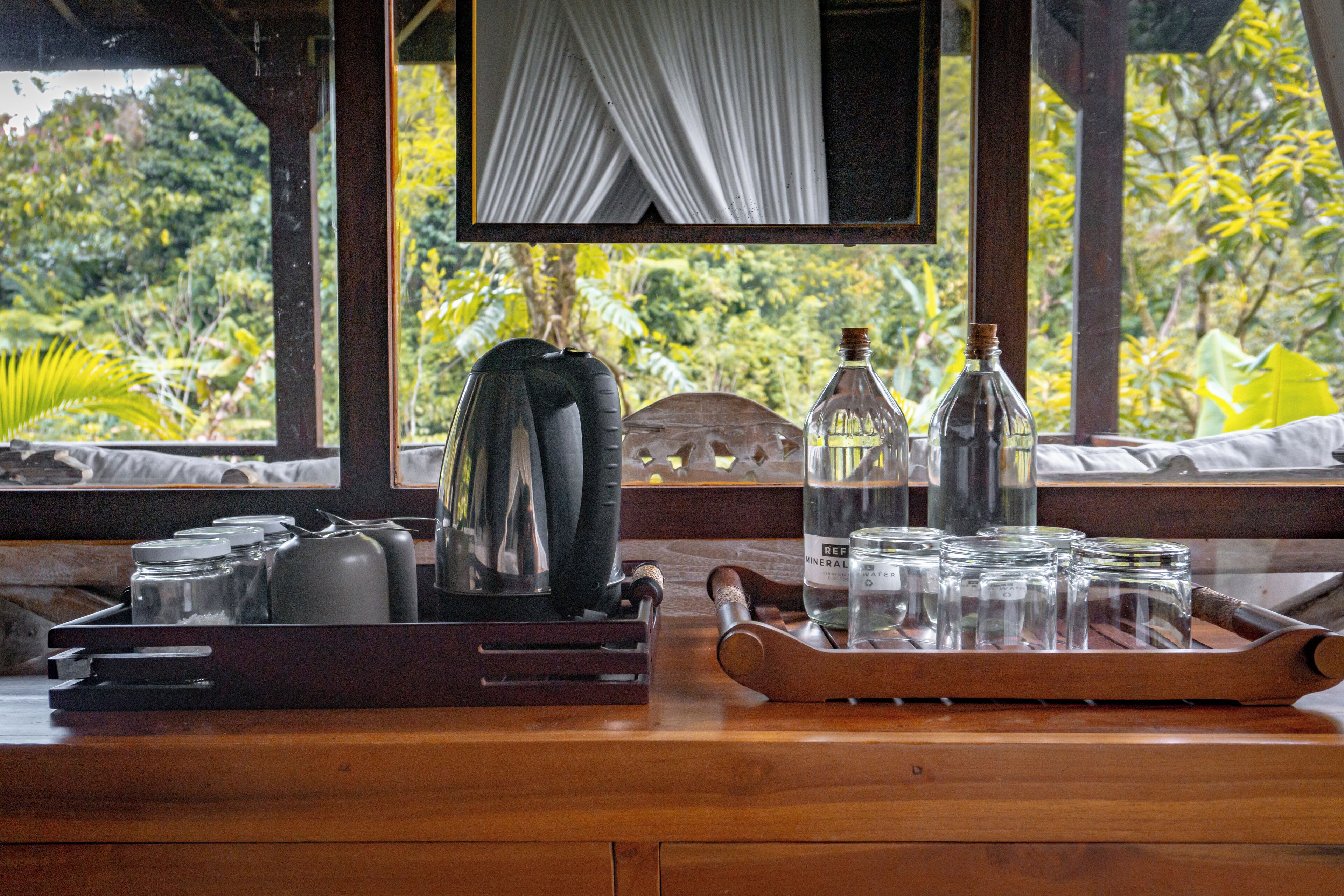 Ein Holztisch mit einer Tablettplatte, auf der Geschirr und Glasflaschen stehen, vor einem Fenster mit Blick auf üppiges Grün.