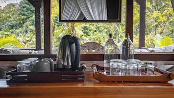 Ein Holztisch mit einer Tablettplatte, auf der Geschirr und Glasflaschen stehen, vor einem Fenster mit Blick auf üppiges Grün.