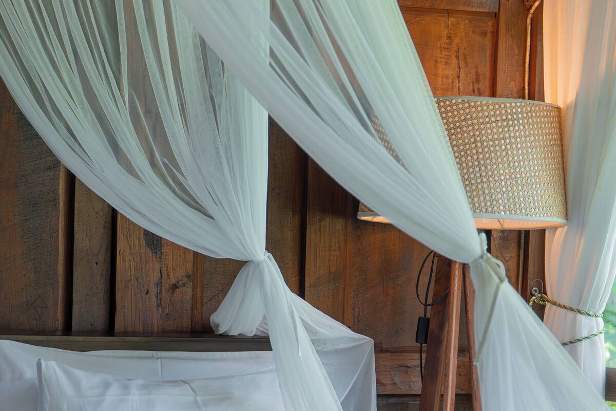 A bed with white linens and a canopy, a wooden wall, and a lamp.