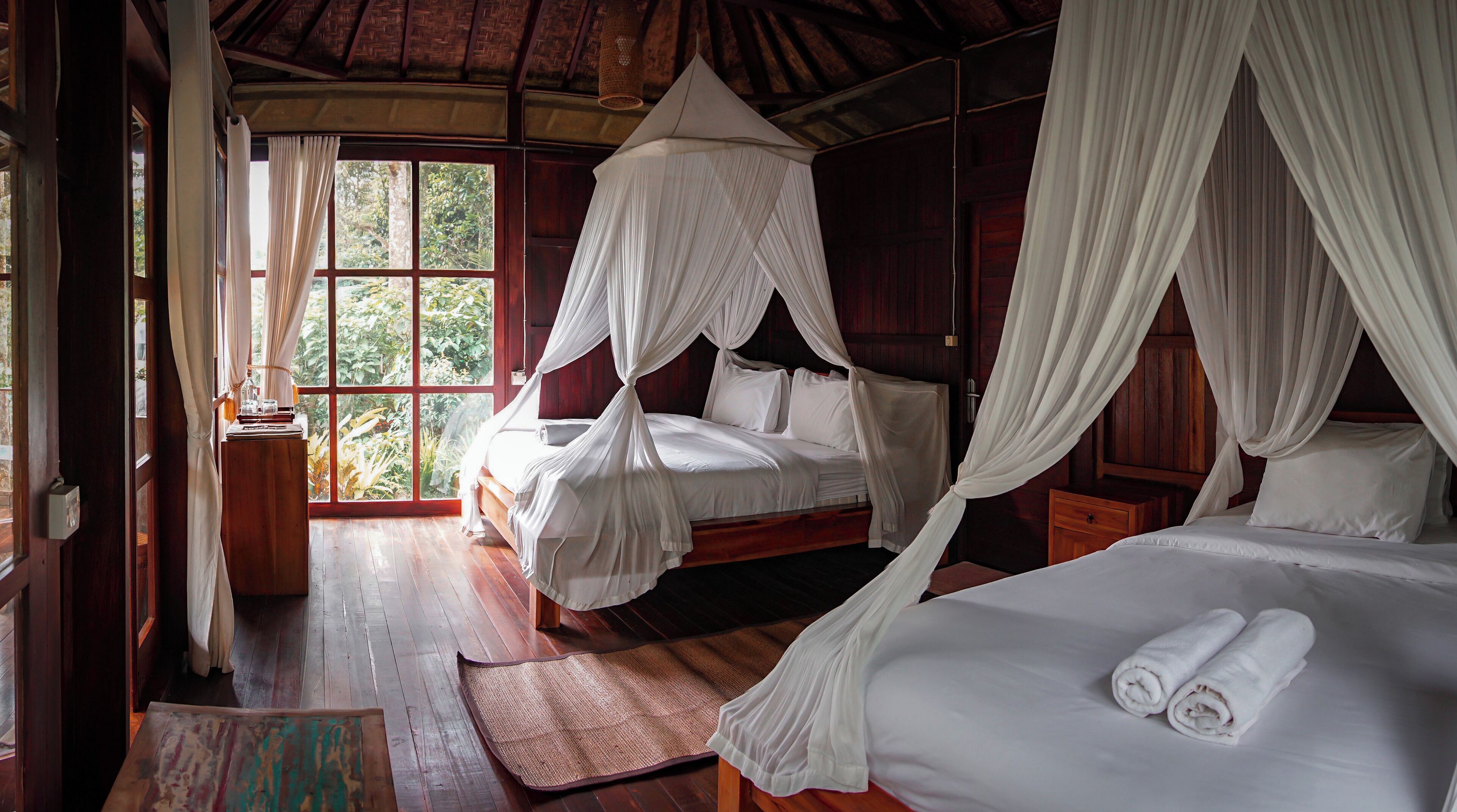 Quarto com cama sob um dossel, janela com cortinas e piso de madeira.