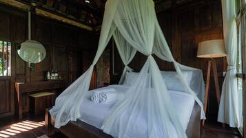 Una habitación de madera con una cama cubierta por un dosel blanco. Hay un banco de madera y una lámpara sobre una mesita.