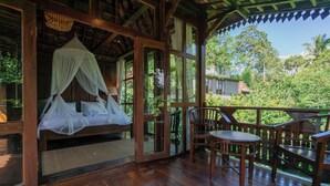 A wooden deck with a bed and chairs, surrounded by lush greenery. - Kebun Kita Ecolodge (Pupuan)