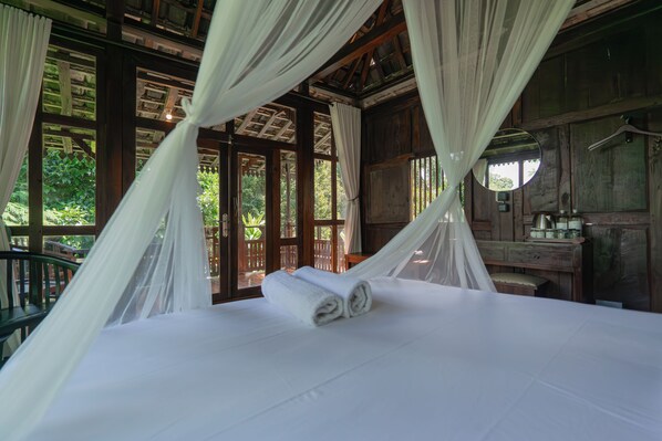 A bed with white linens and a rolled towel, a wooden dresser, and a mirror on the wall. - Kebun Kita Ecolodge (Pupuan)