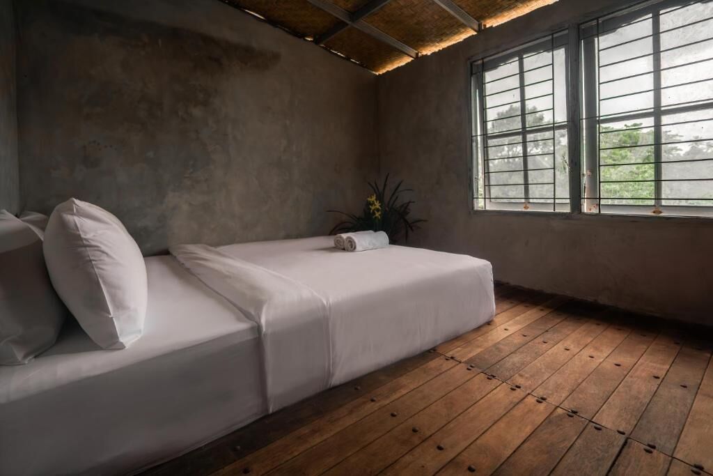 A room with a wooden floor, a white sofa with pillows, a potted plant, and a window with blinds.