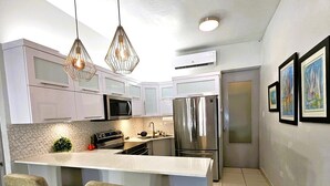 A modern kitchen with a central island, bar stools, pendant lights, and stainless steel appliances. - Saldana Townhouse (San Juan)