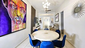 A modern dining area with a round table, blue chairs, a ceiling fan, and a large abstract painting on the wall. - Saldana Townhouse (San Juan)