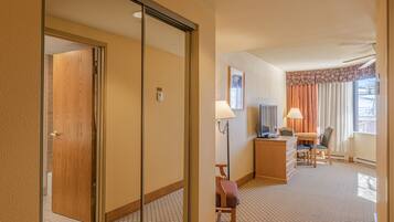 Ett hotellrum med en dörr av trä, ett skrivbord med en stol, en tv och ett fönster med gardiner.