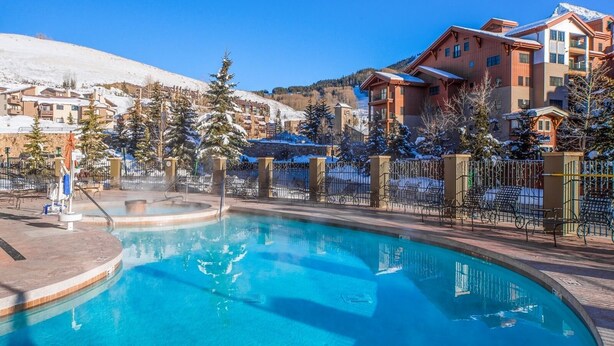 A pool area with a clear blue pool, surrounded by a fence and lounge chairs. - Crested Butte Mountain Resort (Crested Butte)