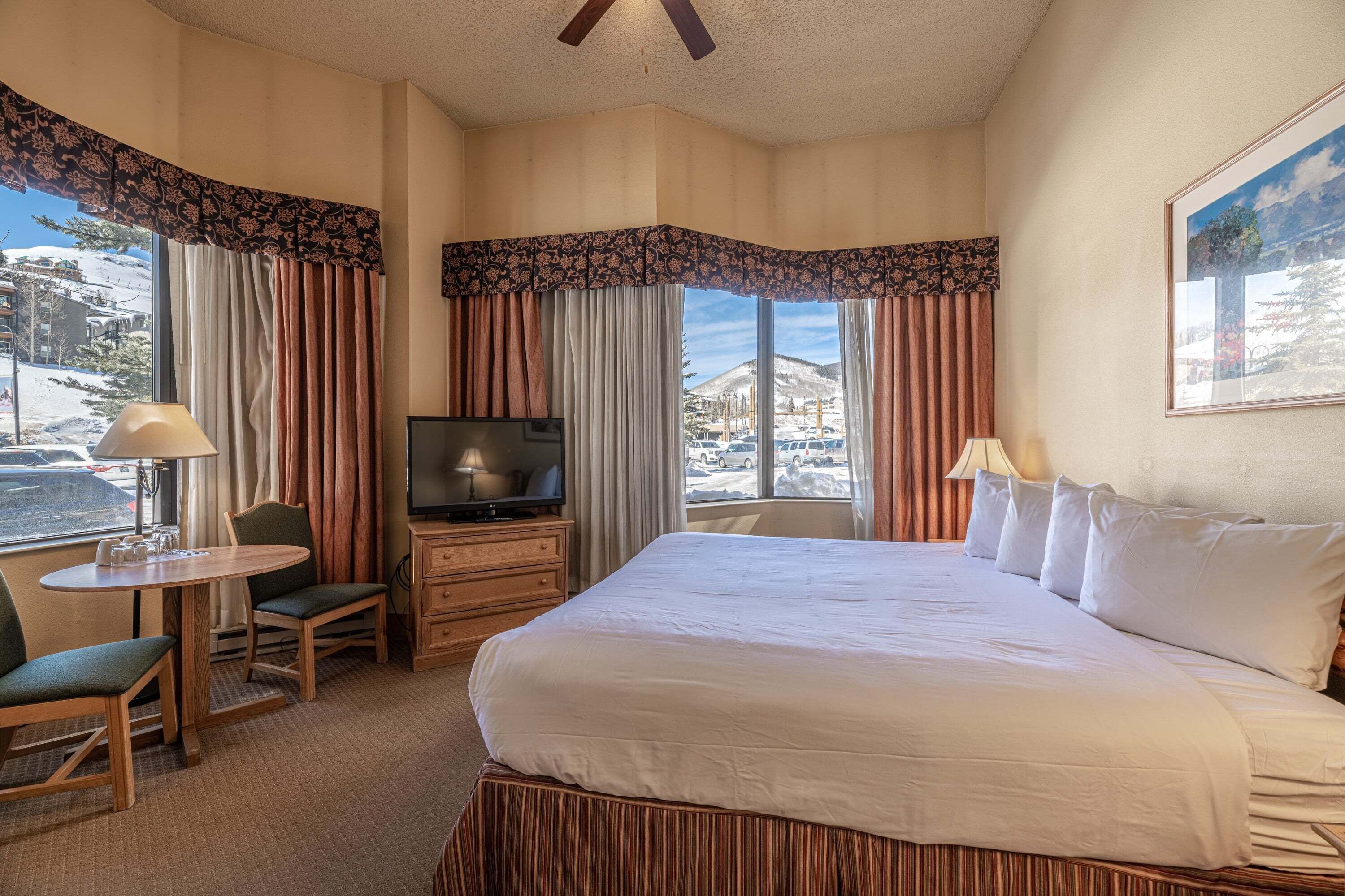 A hotel room with a large bed, a desk with a chair, a television, and a window with curtains.