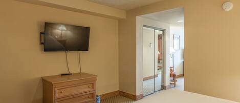 A hotel room with a flat-screen TV mounted on the wall, a wooden dresser, a ceiling fan, and a large bed.