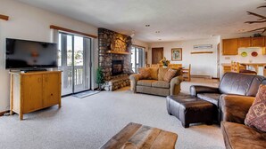 A spacious living room with a stone fireplace, a television on a wooden cabinet, and a comfortable seating area with a leather couch and ottoman. - Crested Butte Mountain Resort (Crested Butte)
