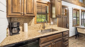 A kitchen with wooden cabinets, a granite countertop, a coffee maker, and a window with blinds.
