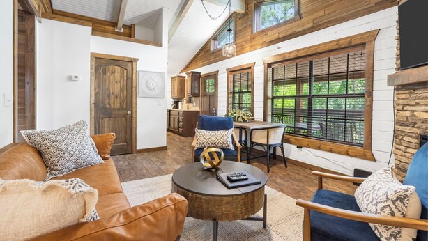 A spacious living room with a brown leather couch, a round coffee table, and a dining area with a table and chairs.