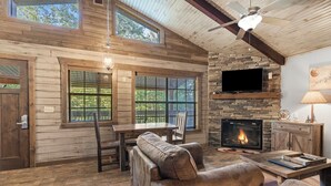 A cozy living room with a stone fireplace, wooden walls, and large windows. - Table Rock Lakeside cabin -Ticket Deals & Resort Perks included! (Branson)