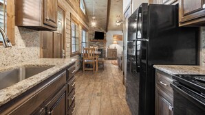 A kitchen with granite countertops, wooden cabinets, a black refrigerator, and a stone fireplace. - Table Rock Lakeside cabin -Ticket Deals & Resort Perks included! (Branson)