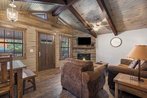 Un interior de cabaña acogedor con paredes de madera, una chimenea, un televisor y un comedor.