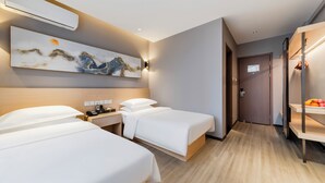 Habitación de hotel con dos camas, aire acondicionado de pared, un cuadro, una mesita de noche con un teléfono y un armario con una cesta de fruta.