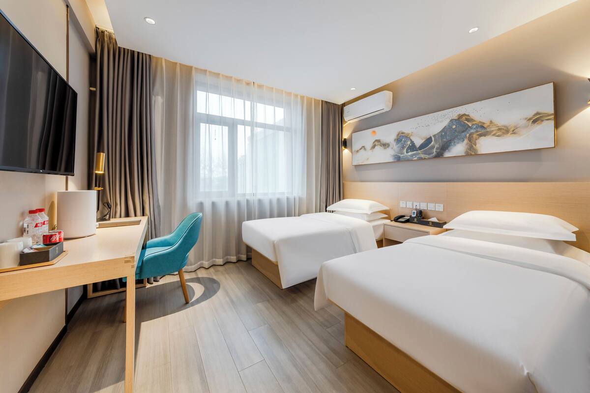 Una habitación de hotel con dos camas, un escritorio, una silla, un televisor y un cuadro en la pared.