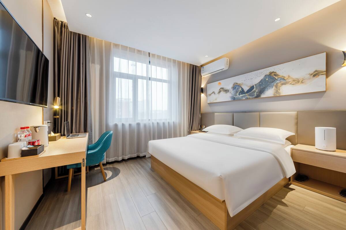 Una habitación de hotel moderna con una cama grande, un escritorio con una computadora portátil, un televisor y un cuadro en la pared.