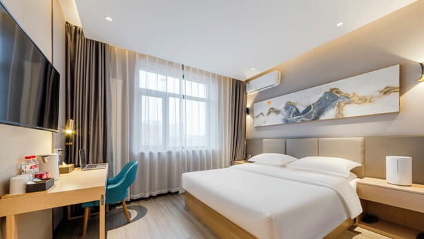Una habitación de hotel moderna con una cama grande, un escritorio con una computadora portátil, un televisor y un cuadro en la pared.