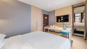 Una habitación de hotel moderna con una cama grande, un escritorio con silla, un televisor y un armario.
