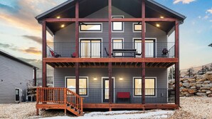 A two-story building with a balcony on the second floor, a staircase leading to the entrance, and a stone wall in the background. - Spacious Family Retreat | Free Boat Slip + Show Tickets (Branson)
