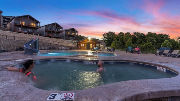 A resort with multiple swimming pools, a slide, and a building with a warm light. - Spacious Family Retreat | Free Boat Slip + Show Tickets (Branson)