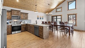 A modern kitchen with wooden cabinets, stainless steel appliances, and a large island with bar stools. - Spacious Family Retreat | Free Boat Slip + Show Tickets (Branson)
