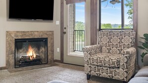 Una sala de estar con chimenea, un televisor montado encima y un sillón estampado.