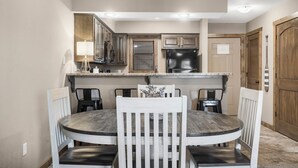Un comedor con una mesa redonda y cuatro sillas, una cocina con armarios de madera y un refrigerador negro, y una puerta de madera con manija.
