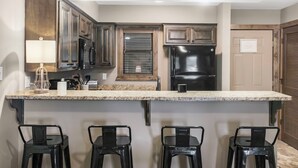 Una cocina con armarios de madera oscura, un refrigerador negro, una encimera de mármol y cuatro taburetes negros.
