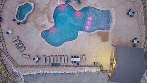 Vista aérea de una zona de piscina con varias piscinas, sillas de descanso y una zona de estar cubierta.